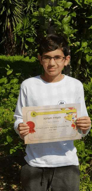 a young boy holds up a certificate with a red ribbon