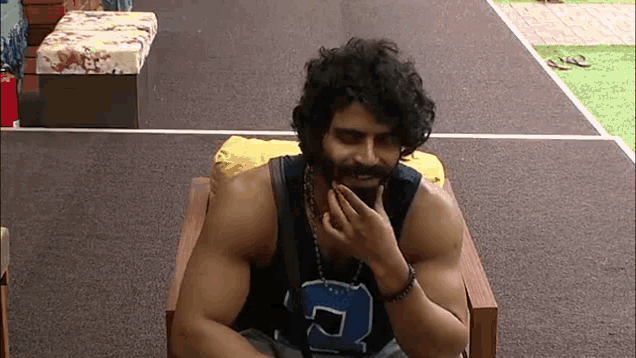 a man with curly hair and a beard is sitting in a chair with his hand on his face .
