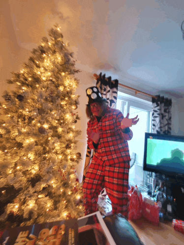 a person standing in front of a christmas tree wearing a plaid pajamas