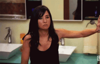 a woman in a black tank top is taking a selfie in a bathroom with two sinks .