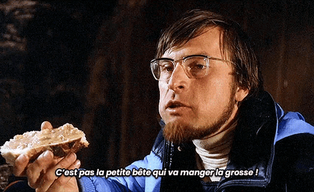 a man with glasses is holding a piece of bread and says c'est pas la petite bete