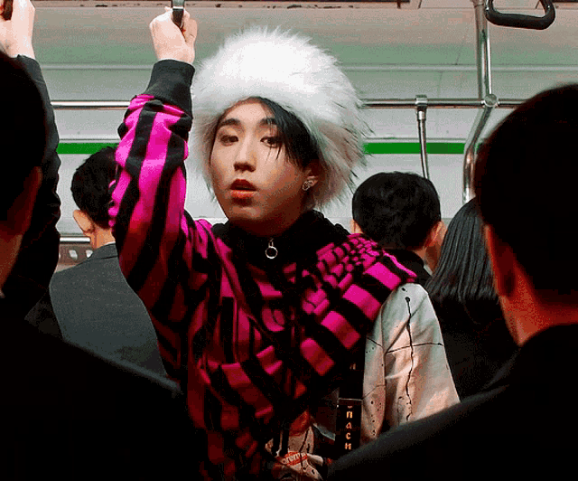 a woman wearing a pink and black striped shirt and a white fur hat holds onto a railing