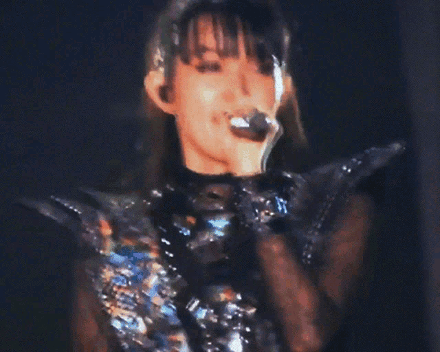 a close up of a woman singing into a microphone with the letter t on her wrist