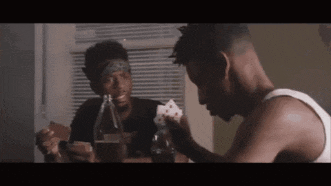 a man in a bandana is holding a bottle and playing cards with another man