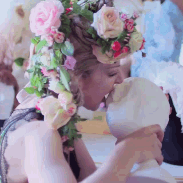 a woman wearing a flower crown kisses a statue