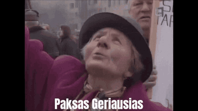 a woman wearing a black hat holds a sign that says paksas geriausias