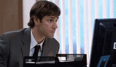 a man in a suit and tie is sitting at a desk in front of a computer monitor .
