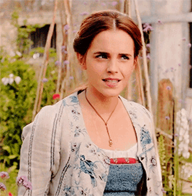 a woman wearing a floral cardigan and a necklace is standing in a garden
