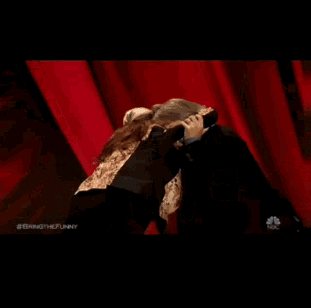 a man and woman are dancing on a stage with a red curtain behind them .