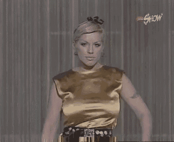 a woman in a gold dress is standing in front of a curtain .
