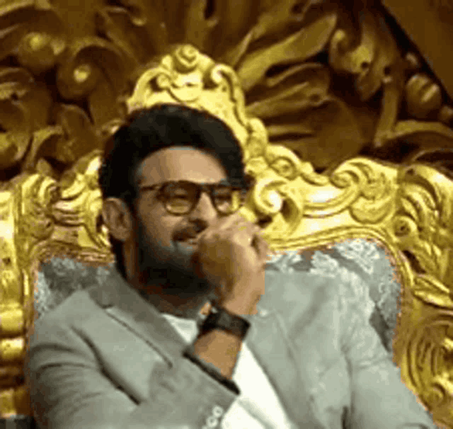 a man in a suit and glasses is sitting in a chair with his hand on his face .