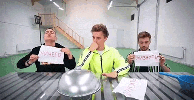 a group of young men are sitting at a table holding signs in russian .