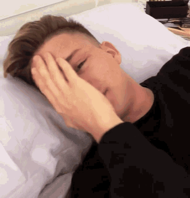 a young man laying on a bed with his hand on his forehead