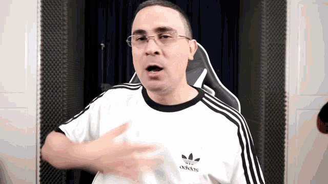 a man wearing glasses and a white adidas shirt is making a funny face