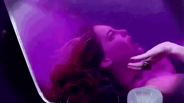 a woman with red hair is laying in a bathtub with purple lights .