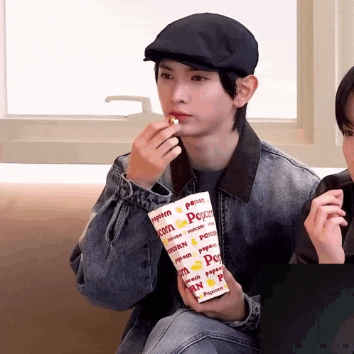 a young man is eating popcorn from a container that says popcorn