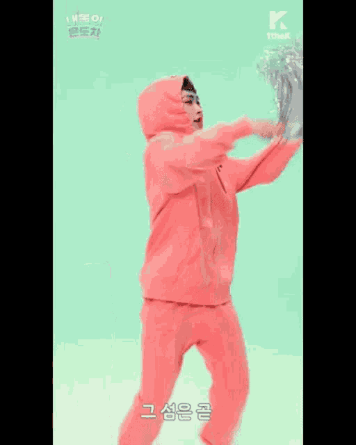 a man in a pink hoodie and pink sweatpants is holding a cheerleader pom pom .