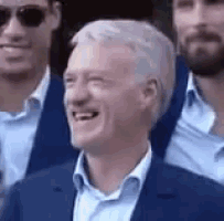 a man in a blue suit and white shirt is laughing while sitting in a crowd of people .
