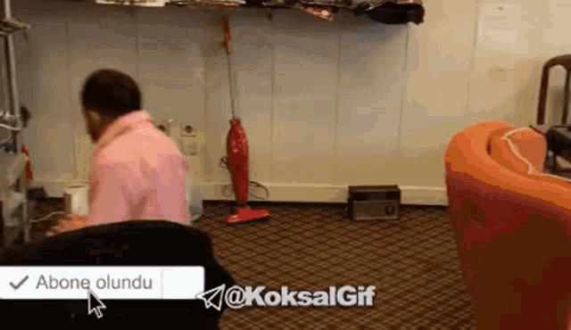 a man in a pink shirt is sitting in a chair with a vacuum cleaner in the background .