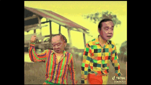 two men in colorful shirts are standing in front of a building .