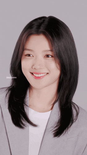 a woman with long black hair is smiling and wearing a grey suit jacket