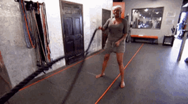 a woman is standing on a gym floor holding a rope .
