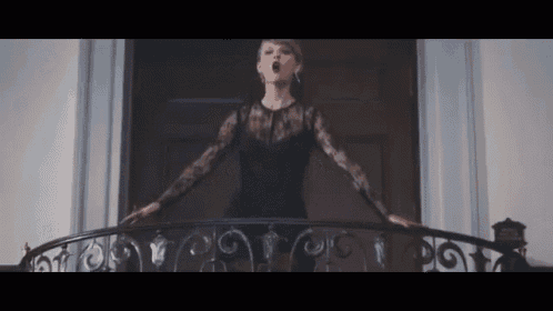 a woman in a black lace dress is standing on a balcony .