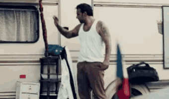 a man in a white tank top is standing in front of a white trailer