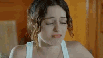 a woman in a white tank top is crying with her eyes closed and her mouth open .