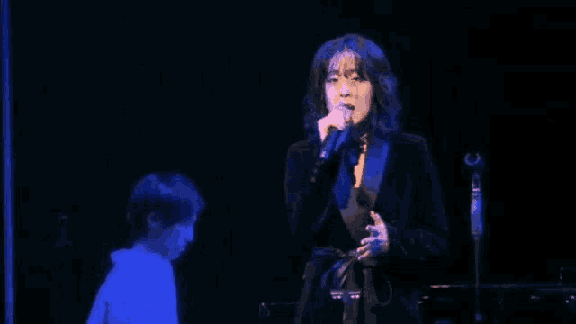 a woman is singing into a microphone on stage while a man plays a piano .