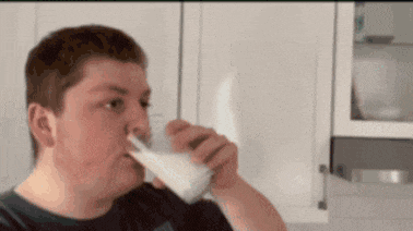 a man is drinking a glass of milk from a carton .
