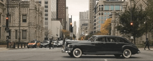 a black car with white tires is driving down a busy city street