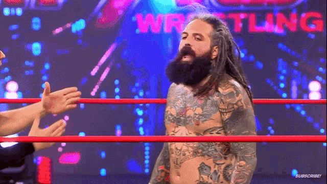 a man with dreadlocks and tattoos is in a wrestling ring with the word wrestling behind him