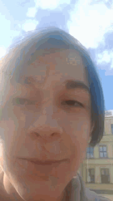 a close up of a person 's face with blue hair and a building in the background .