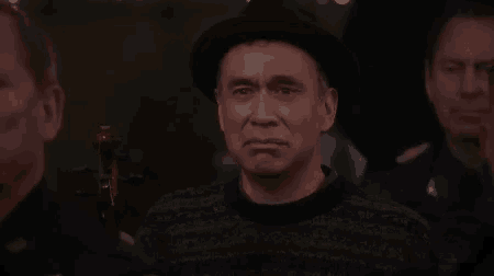 a man wearing a hat and a sweater is sitting in a crowd .