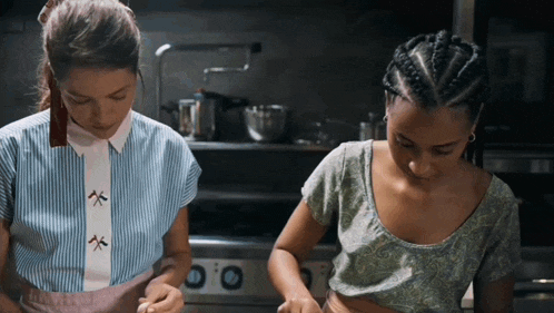 two women are cooking in a kitchen and one has braids on her hair