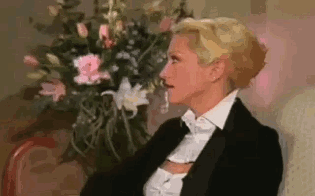 a woman in a tuxedo is sitting next to a vase of flowers .