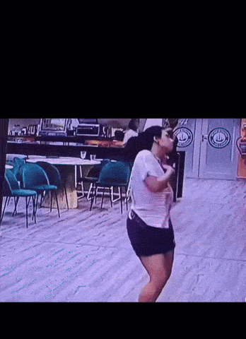 a woman in a white shirt and black shorts is dancing in a room with a sign that says ' a & b '