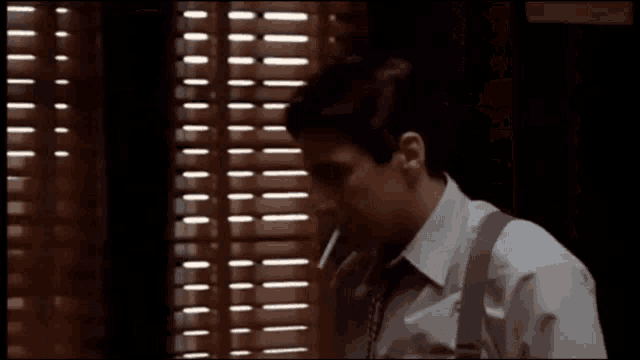 a man smoking a cigarette and saying she 's hysterical in front of a window