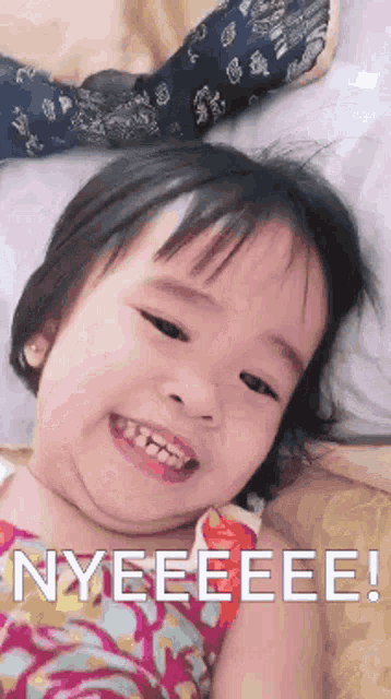 a little girl is smiling and laying on a bed with the words nyeeeee written on the bottom