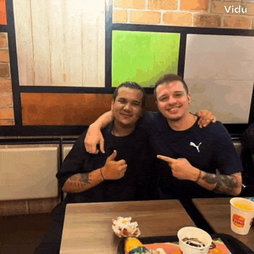 two men are sitting at a table with a burger king cup in front of them