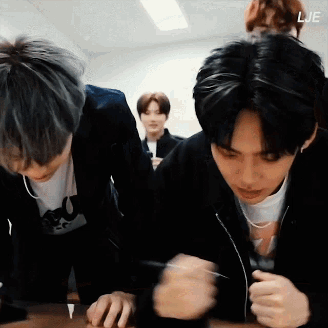 a group of young men are sitting around a table and one of them is wearing a necklace that says lje