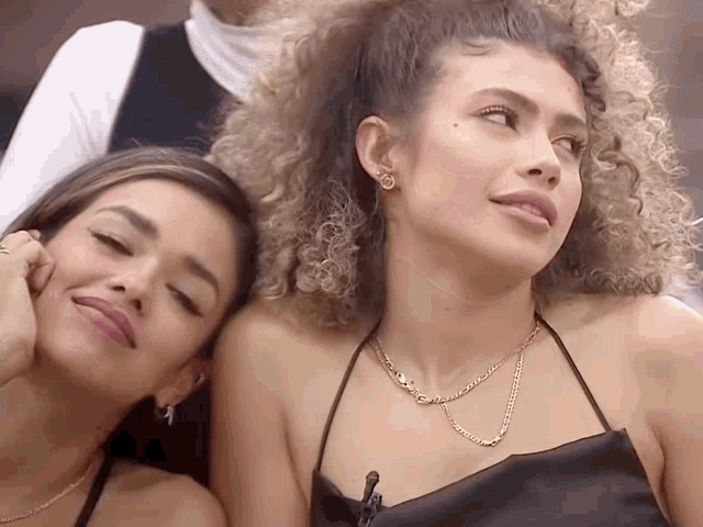 two women sitting next to each other with one wearing a necklace