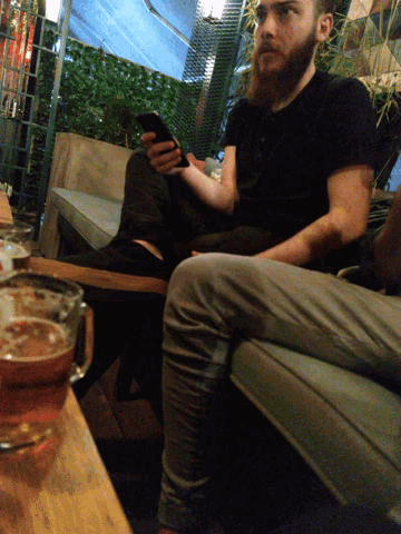 a man with a beard sits at a table with a glass of beer in front of him
