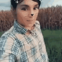 a young boy is taking a selfie in a field with a cat mask on his face .