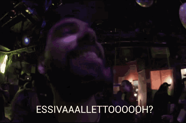 a man with a beard is smiling in a dark room with the words " essivaaaellettooooh " written above him