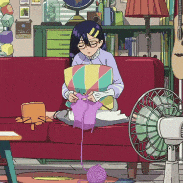 a girl sits on a red couch knitting a sweater