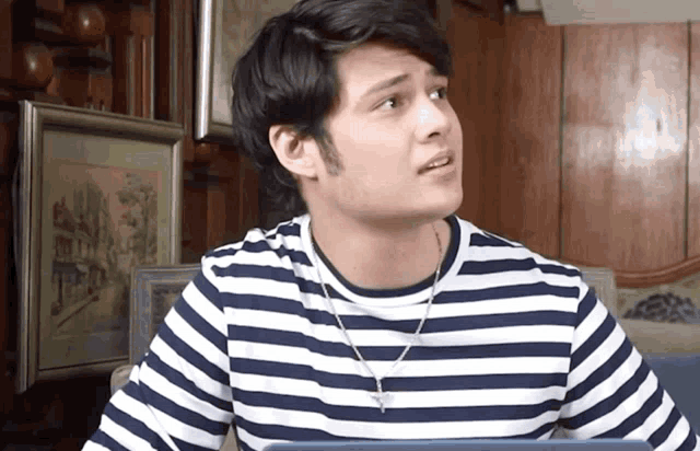 a man wearing a striped shirt and a necklace looks up at something