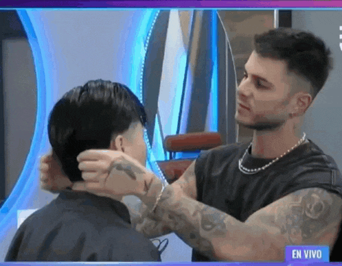 a man is cutting another man 's hair in front of a blue sign that says en vivo