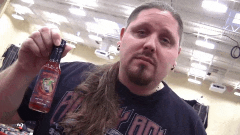 a man with long hair is holding a bottle of hot sauce that says ' scorpion ' on it